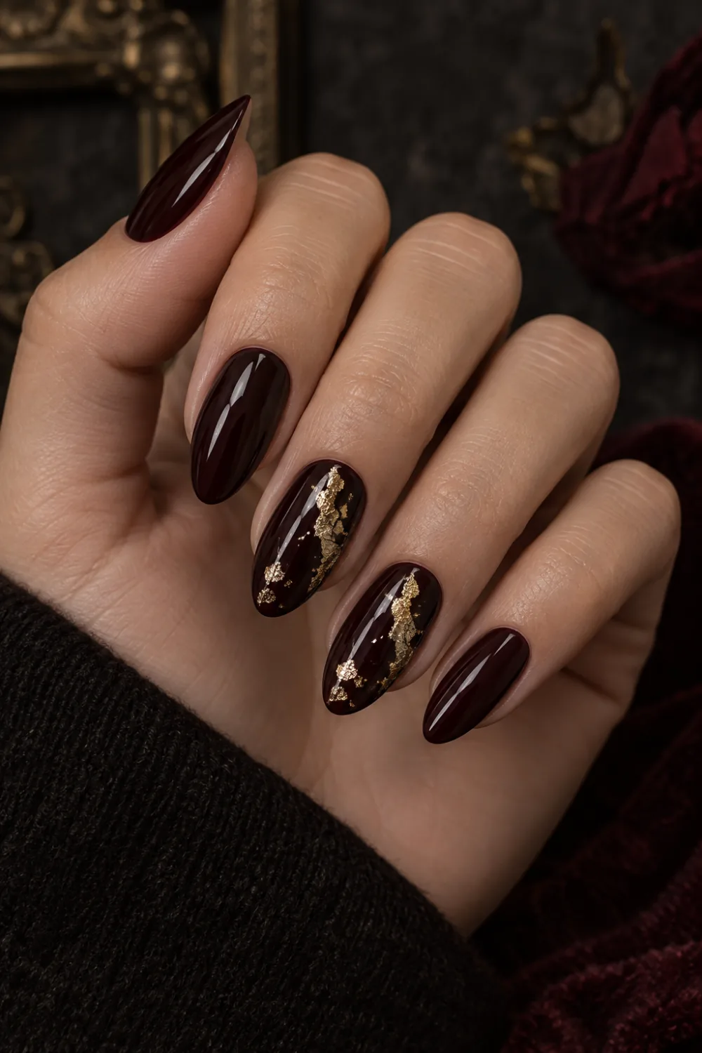Deep burgundy almond nails with irregular gold foil accent fragments