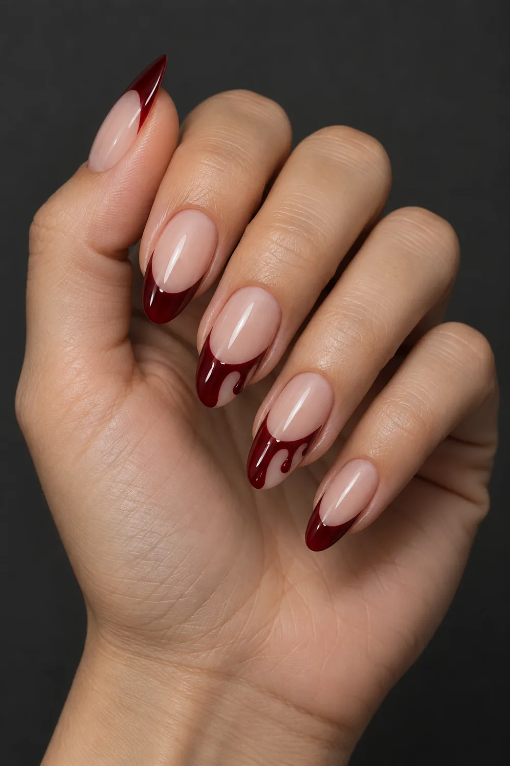 Nude almond nails with dark red French tips and painted drip accents
